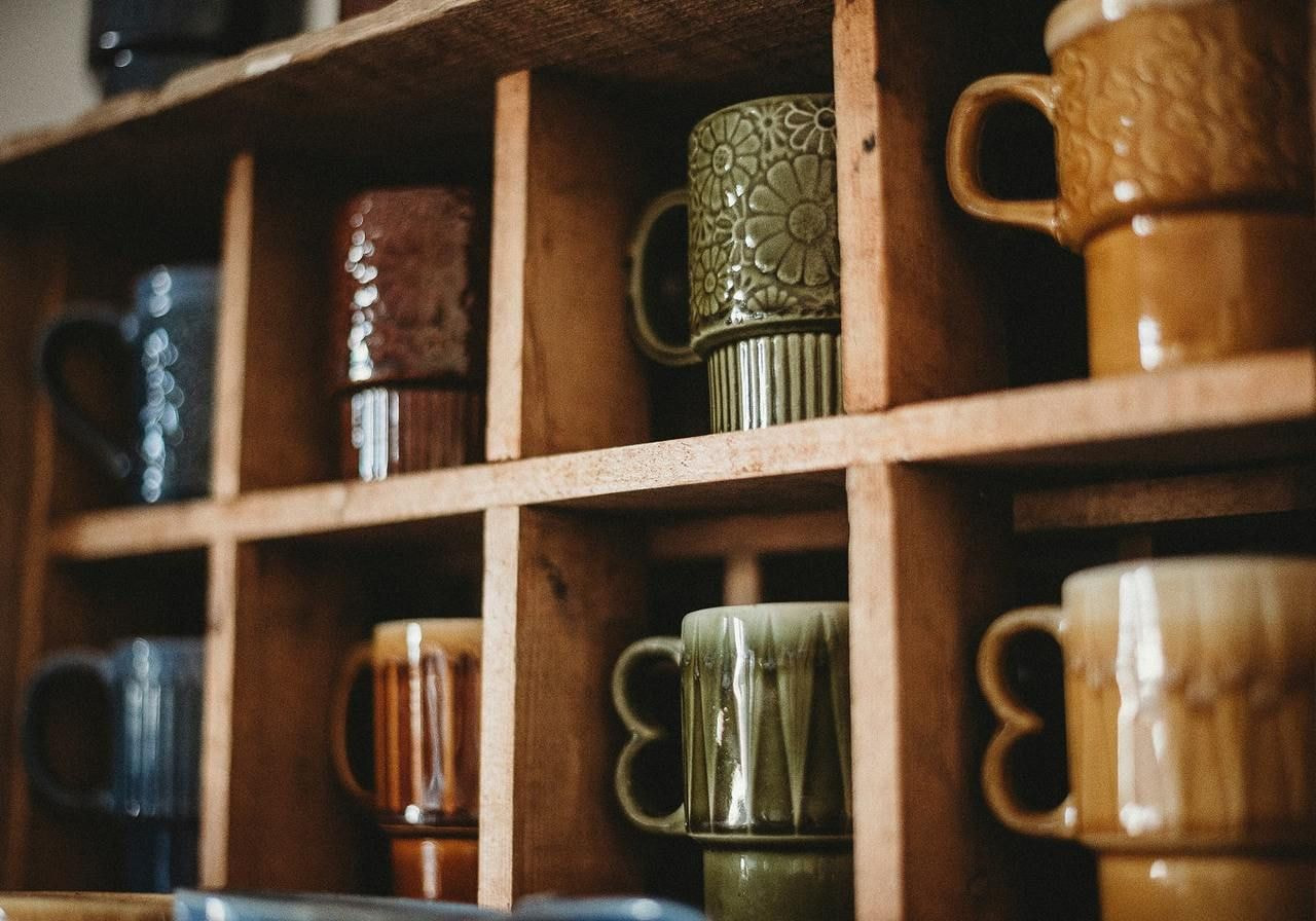 A wooden shelf displaying a variety of colorful coffee mugs arranged neatly.